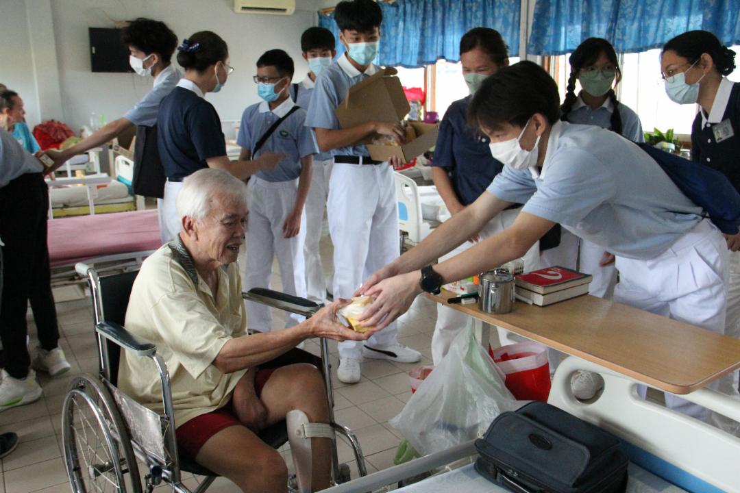 慈少班学员把饮料和蛋糕伴手礼恭敬地递给长者。 【摄影：谭志雄】