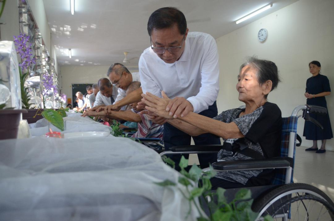 志工协助长者们合十，依序完成“礼佛足、接花香、祝福吉祥”的浴佛仪式，恭敬而庄重。 【摄影：陈敬德】