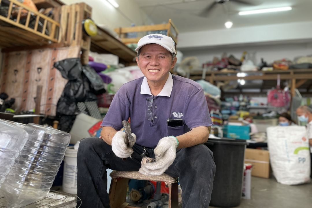 戴着慈济帽的黄文吉坐在改造的小木凳上，笑对人生；身上泛白的慈济制服，道尽他在慈济菩萨道上十三年的岁月。 【摄影：陈馨如】