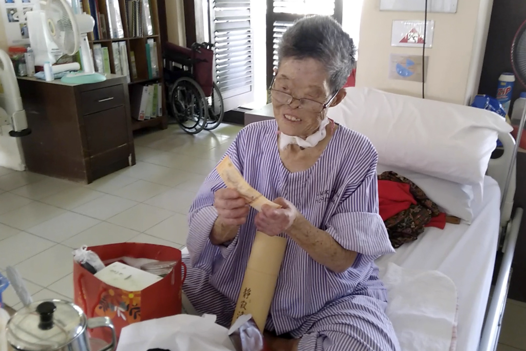 Grandma Heng took a RM20 note from a red packet and put it into her new coin bank. She hopes to save more and donate the contents when it is completely filled. [Photo by Wee Yong Ching]